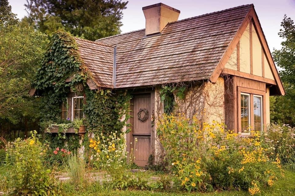Cottage at Raspberry Hill surrounded by flowers and green foliage.